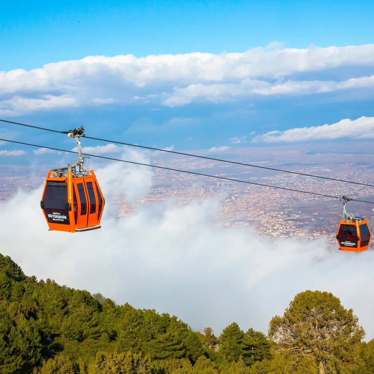 Denizli cable car cabins above a sea of cloud with the city below